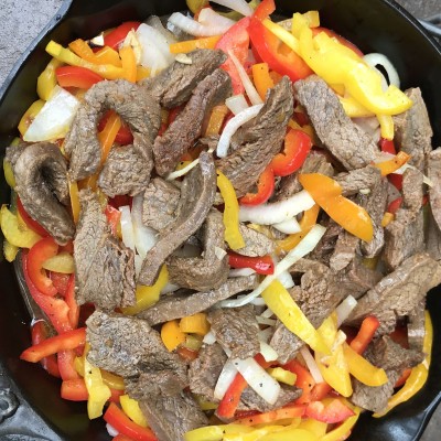 meat, peppers, and onions in a cast iron pot